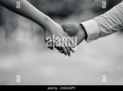 Un'immagine in scala di grigi di una sposa e uno sposo che tiene le mani Foto Stock