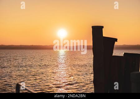 Splendido tramonto sullo splendido Lago di Garda in Italia, con il sole che si riflette sulle acque calme e crea un'atmosfera tranquilla. Perfetto per chi viaggia Foto Stock