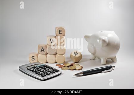 Home finanza concetto durante l'inflazione, cubi di legno con la parola salvare e un segno di percentuale, piggy bank, calcolatrice e alcune monete su un dorso grigio beige Foto Stock