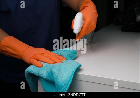 primo piano delle mani della donna in guanti di gomma arancione per la pulizia della superficie bianca del comò. pulizia della molla . Foto di alta qualità Foto Stock