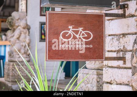 Pedalare lentamente - persone che attraversano la piccola strada o la strada segnale di avvertimento stradale a Sanur, Bali Foto Stock