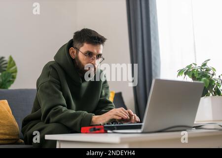 Uomo produttore di musica o arrangiatore utilizzando computer portatile e tastiera midi e altre apparecchiature audio per creare musica in casa studio. Battete facendo e organizzando Foto Stock