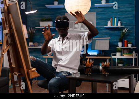 Artista afro-americano alla ricerca di ispirazione nell'universo online con occhiali per realtà virtuale presso lo studio di home art. Giovane studente di disegno alla ricerca di nuove tecniche artistiche a meta VERSE. Foto Stock