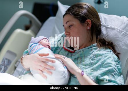 madre e il suo neonato catturati in un ambiente ospedaliero mentre la madre parla sul suo telefono cellulare Foto Stock