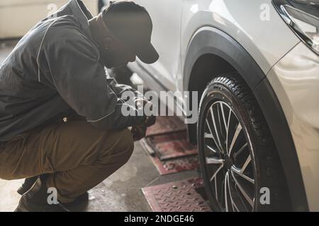 un meccanico che guarda una ruota e ne controlla la geometria presso l'officina di riparazione auto, a colpo pieno. Foto di alta qualità Foto Stock