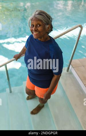 Ritratto di donna anziana afroamericana sorridente mentre si alza sulle scale della piscina. stile di vita e concetto di vita senior in pensione Foto Stock