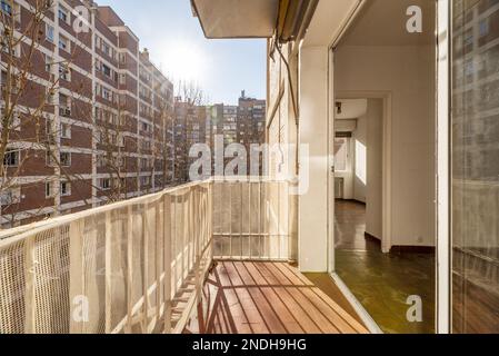 Una terrazza di una casa con grandi finestre in vetro e alluminio che conduce ad un soggiorno vuoto e vista di un patio isolato con altri edifici Foto Stock