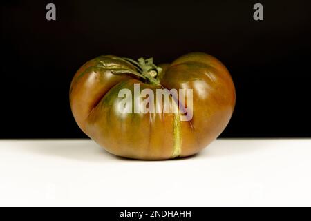 Un delizioso pomodoro solitario maturo della varietà di marmellata dolce su un tavolo bianco sobrio e fondo nero profondo Foto Stock