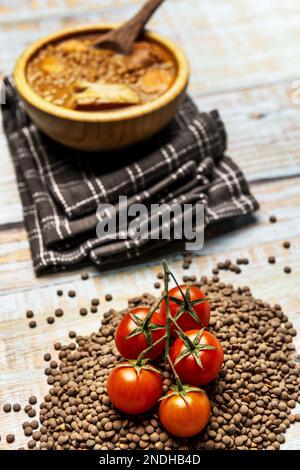 Una vita ferma con grappoli di pomodori ciliegini in cima ad un mucchio di lenticchie secche e uno stufato di lenticchie sullo sfondo Foto Stock