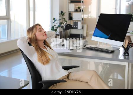 Giovane donna d'affari che si rilassa in sedia da ufficio sul posto di lavoro Foto Stock