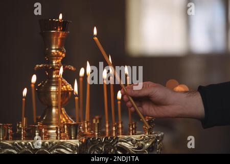 Uomo che illumina candela vicino stand in chiesa, primo piano. Cerimonia del battesimo Foto Stock