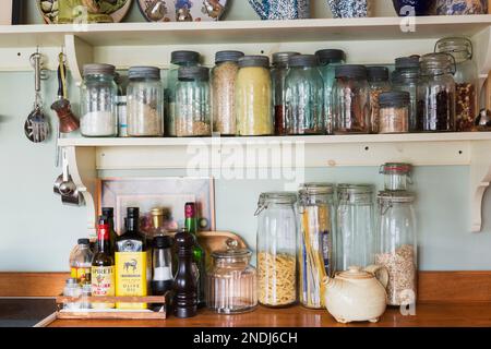 Aromi antichi e vasetti di vetro per spezie su ripiani e ripiani in cucina in stile country all'interno di una vecchia casa del 1650 ristrutturata. Foto Stock