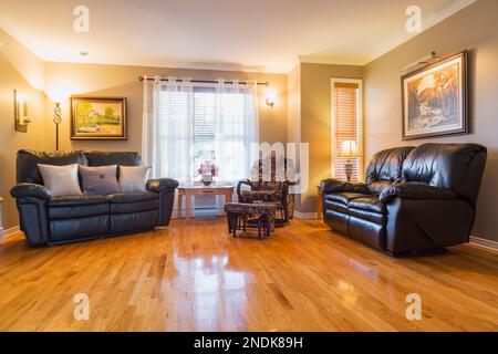 Divani in pelle nera e poltrona reclinabile nel soggiorno con pavimento in legno di quercia all'interno di una casa in stile country. Foto Stock
