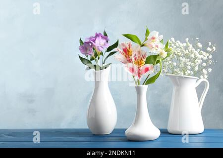 Diversi bei fiori in vasi su tavolo di legno contro sfondo azzurro, spazio per il testo Foto Stock