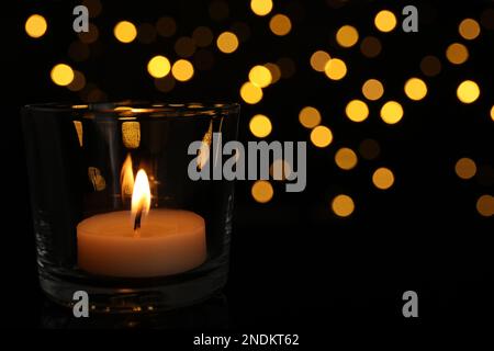 Portabicchieri con candela da tè che brucia contro le luci sfocate nel buio, primo piano. Spazio per il testo Foto Stock