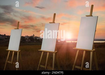 Cavalletto in legno con tele in campo al tramonto Foto Stock