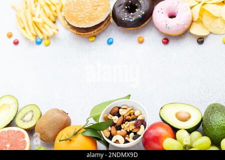 Piatto di cibo sano e malsano da frutta e verdura vs fast food, dolci e pasticceria su fondo grigio cemento. Dieta e detox contro Foto Stock