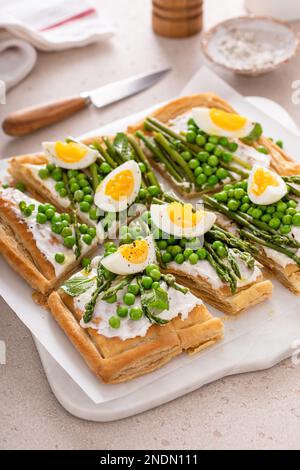 Crostata di primavera fresca con piselli verdi, uova sode e asparagi su pasta sfoglia tagliata a pezzi Foto Stock