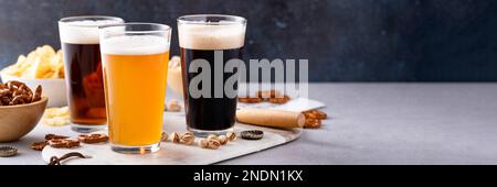 Varietà di birra con stout scuro, lager tradizionale e bianco belga servito con spuntini sul tavolo con spazio copia Foto Stock