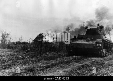Un carro armato di modello T 26 C sovietico catturato del 1937 con le marcature tedesche della Divisione 'Totenkopf' di Panzer SS 3rd guida attraverso un villaggio in fiamme vicino al lago Ilmen. Foto Stock