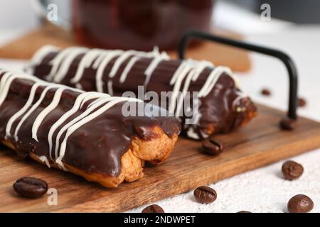 Sali a bordo con deliziose eclair di cioccolato e chicchi di caffè su un tavolo bianco Foto Stock