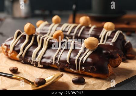 Pergamena con deliziose eclarie al cioccolato, nocciole e chicchi di caffè su tavola di legno nero Foto Stock