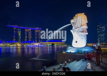 Marina Bay a Singapore visto di notte con il Merlion (simbolo nazionale di Singapore) in primo piano e il Marina Bay Sands Hotel sullo sfondo. Foto Stock