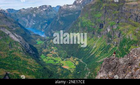 Un uomo in cima al Monte Dalsnibba gode di una vista mozzafiato sulla cima innevata della montagna, Geiranger e Geirangerfjord, in Norvegia. Foto Stock