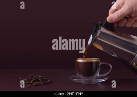 Mans versare il caffè caldo fresco da una moka in una tazza di vetro. Sfondo con spazio di copia. Foto Stock