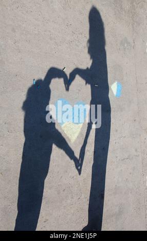 ombre contrastanti di adulto e bambino, cuore giallo-blu abbracciante disegnato con pastelli sul marciapiede. Gli ucraini vogliono la pace. Infanzia durante la guerra. Lo Foto Stock