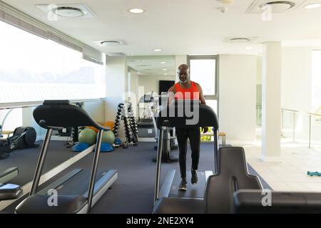 Uomo anziano afroamericano che cammina su un tapis roulant presso la palestra. stile di vita e concetto di vita senior in pensione Foto Stock