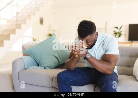 Triste afro-americano seduto sul divano in soggiorno. Trascorrere il tempo di qualità a casa, la vita domestica e il concetto di stile di vita. Foto Stock