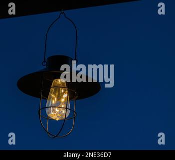 Una lampada a energia solare si illumina a tarda notte sotto il tetto di una casa. Foto Stock