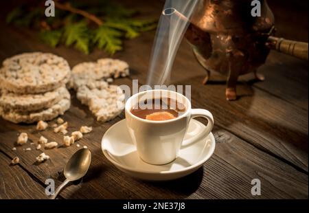 Ancora vita, una tazza di caffè caldo e una caffettiera in piedi su un tavolo di legno illuminato da un raggio di sole del mattino. Foto Stock