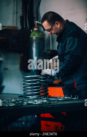 Fabbro in abiti speciali e occhiali di protezione opere in produzione. Lavorazione del metallo con smerigliatrice angolare. Scintille nella lavorazione dei metalli. Foto Stock