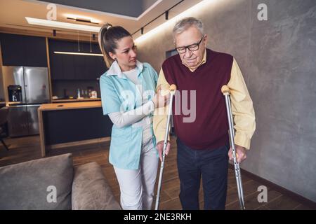L'infermiere che si prende cura di casa sta assistendo l'uomo anziano a casa sua. Assistenza sanitaria professionale per gli anziani. Foto Stock