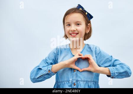 Sorridente bambina fare segno di cuore con le mani in abito denim casual isolato su sfondo bianco, studio, fa l'icona dell'amore, gesto con le dita cuore Foto Stock