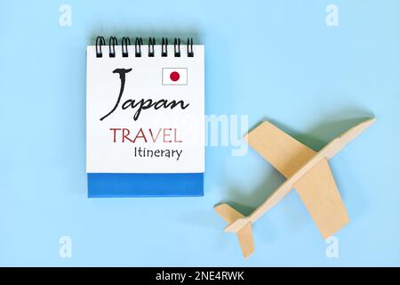 Piano di viaggio o itinerario del Giappone scritto su blocco note blu con bandiera e aereo di legno. Foto Stock