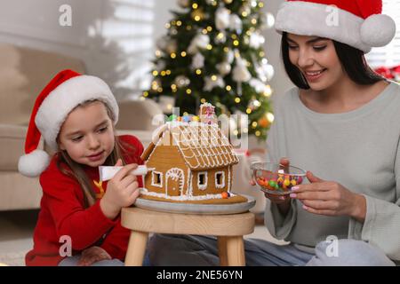 Madre e figlia che decorano casa di pan di zenzero al tavolo al coperto Foto Stock