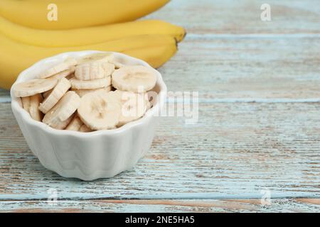Ciotola con banane tagliate vicino alla frutta intera su un tavolo di legno chiaro, primo piano. Spazio per il testo Foto Stock