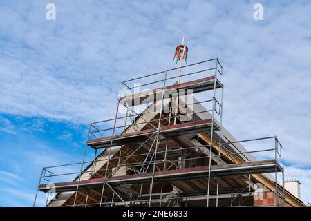 L'ultimo piano di una casa incompiuta con impalcatura e greman tipico può palo o maibaum sul tetto. Cielo blu con nuvole di luce. Foto Stock