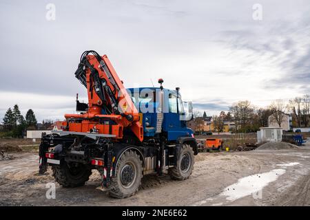 Un'auto con una gru manipolatrice arancione è in piedi in un cantiere. Foto Stock