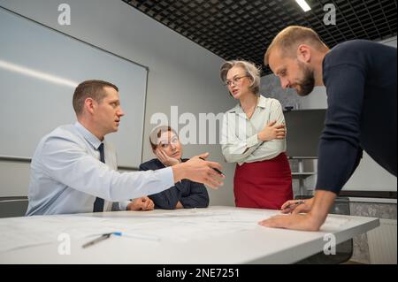 L'estrusione femminile valuta il lavoro dei subordinati. Progettisti ingegneri a una riunione. Foto Stock