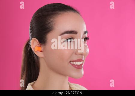 Giovane donna che indossa tappi auricolari in schiuma su sfondo rosa Foto Stock