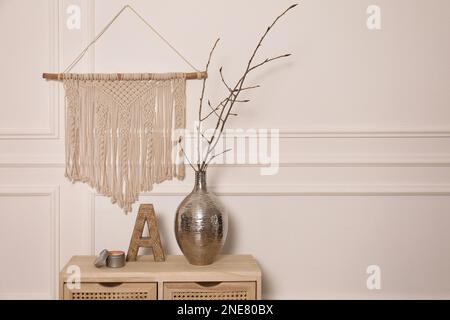 Albero ramoscelli in vaso di metallo e decorazioni su tavolo di legno vicino a parete bianca. Spazio per il testo Foto Stock