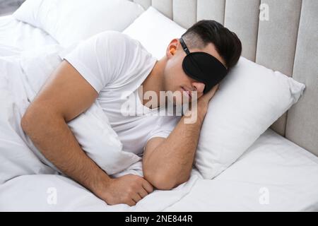 Uomo con tappi auricolari in schiuma e maschera che dorme a letto Foto Stock