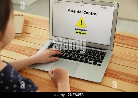 Bambino che utilizza un computer portatile con l'app di controllo genitori installata a casa, primo piano. Sicurezza informatica Foto Stock