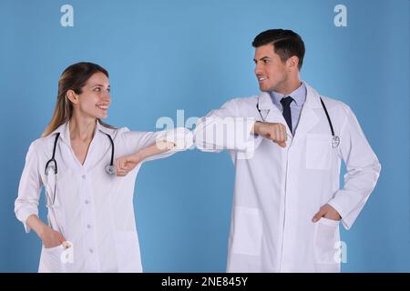 I medici si salutano a vicenda saltando i gomiti invece di fare una stretta di mano su sfondo azzurro Foto Stock