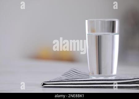 Bicchiere d'acqua e tovagliolo su tavolo bianco su sfondo sfocato. Spazio per il testo Foto Stock