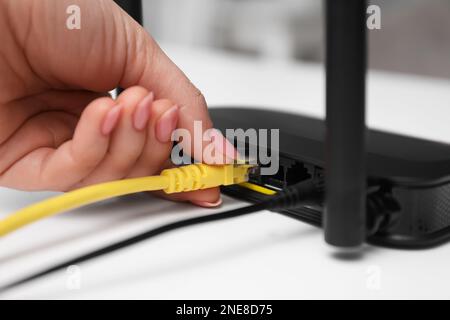 Donna che collega il cavo al router al tavolo bianco, primo piano. Comunicazione Internet wireless Foto Stock